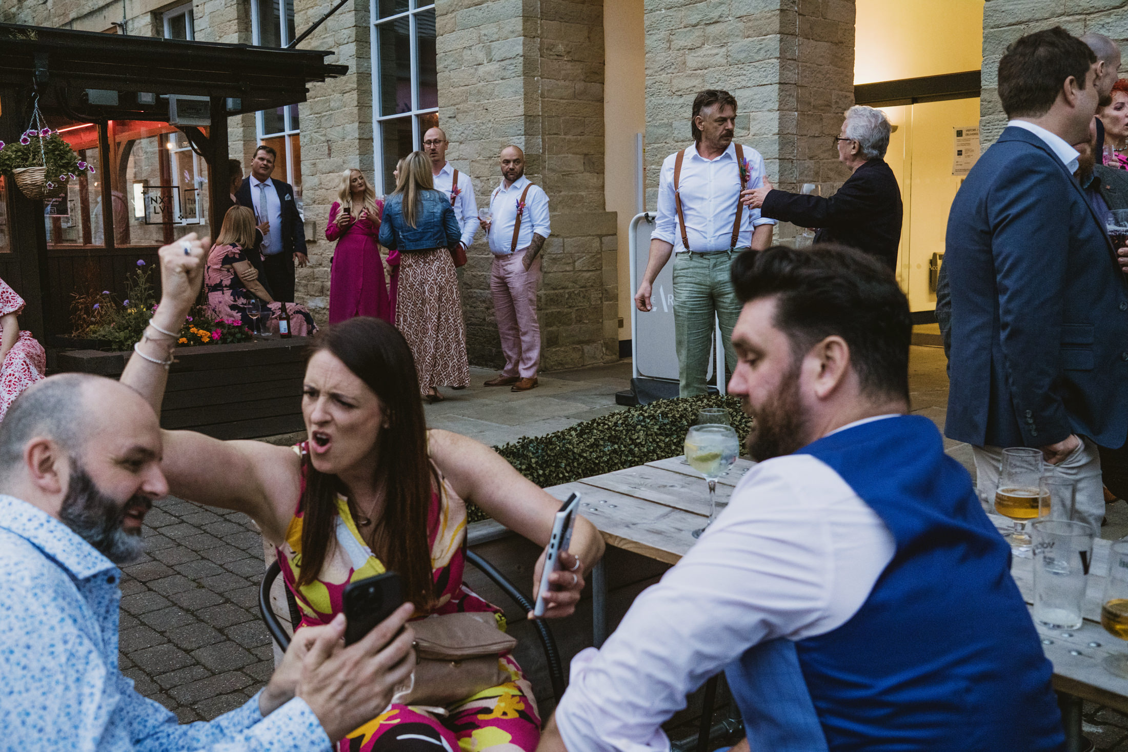 Guests laugh and chat outside stone venue during evening wedding reception drinks