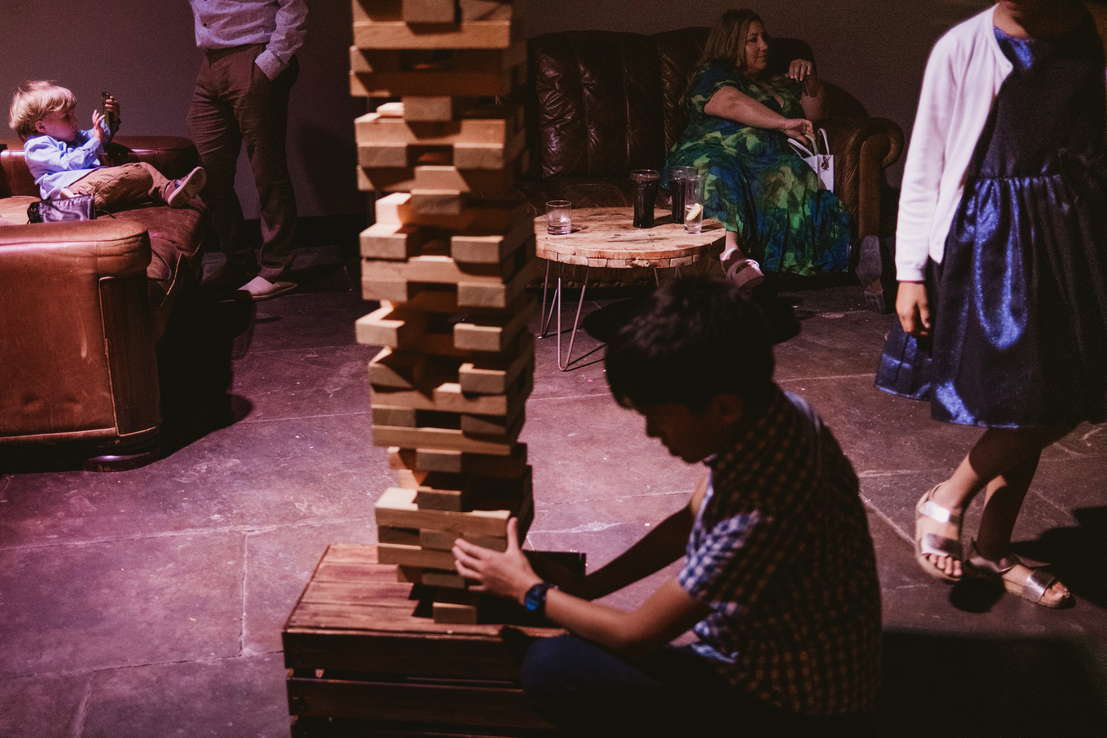 Child concentrates on giant Jenga tower as guests relax nearby at a wedding reception.