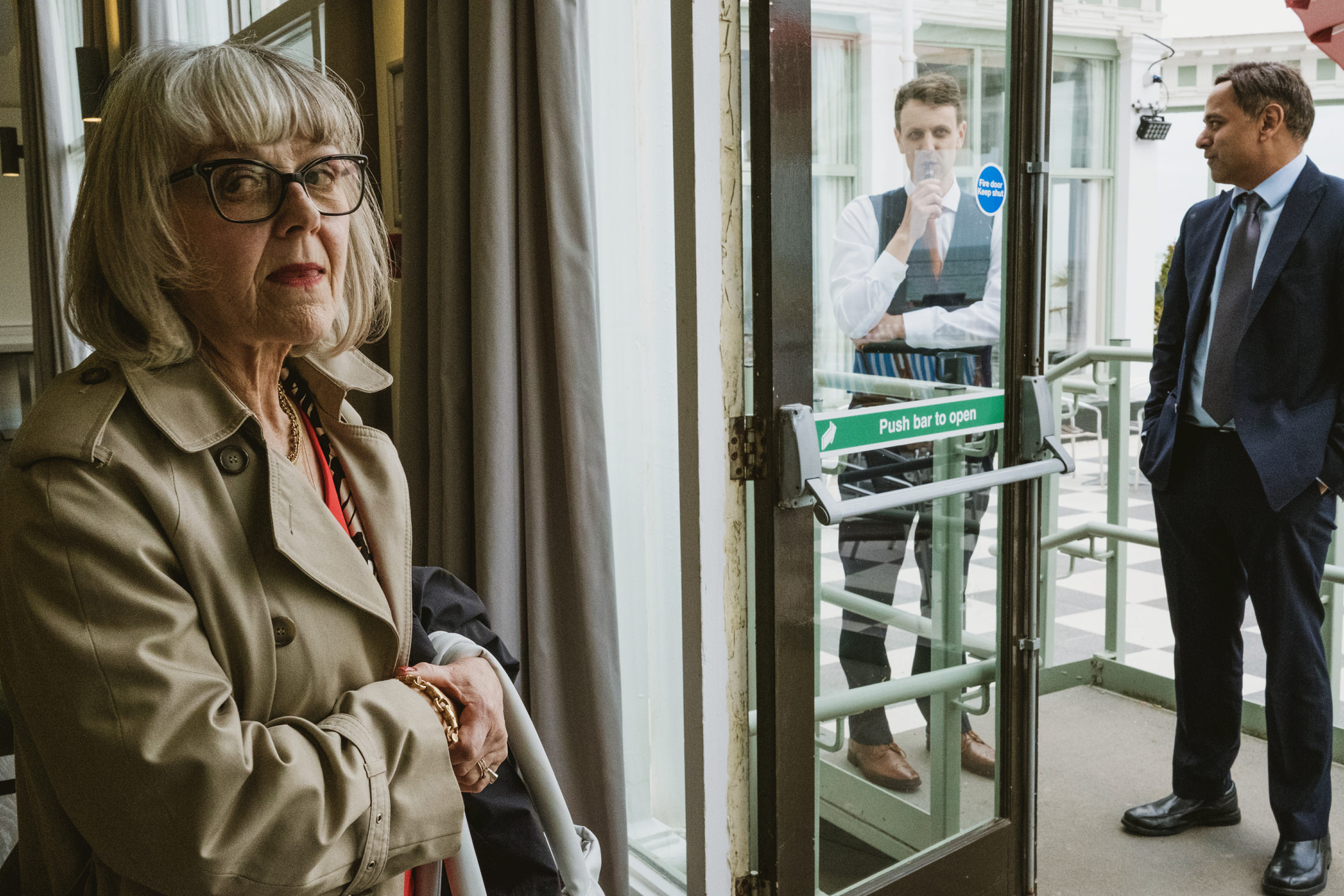 Elderly woman indoors, two businessmen outside.
