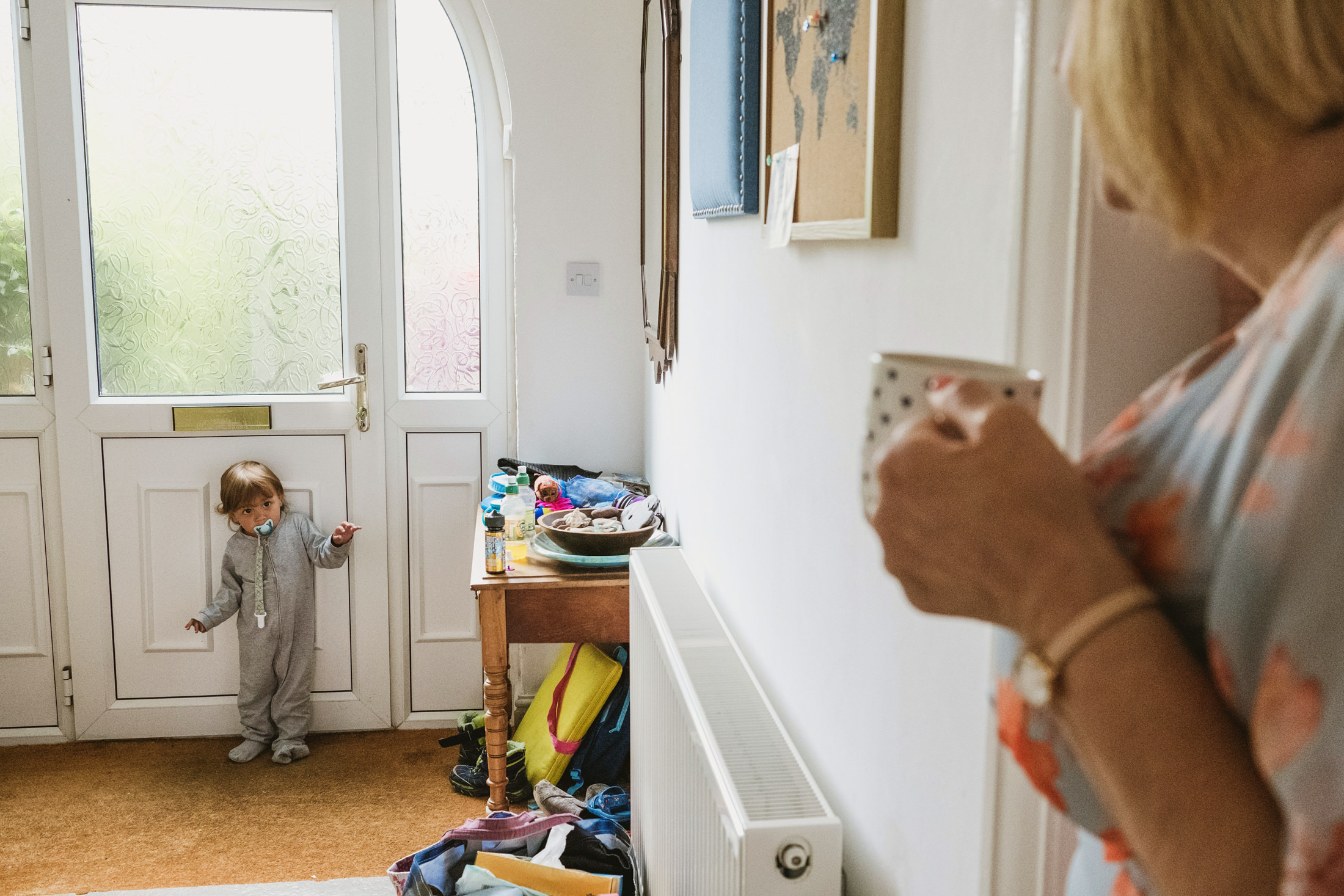Child with dummy near front door, woman watching.