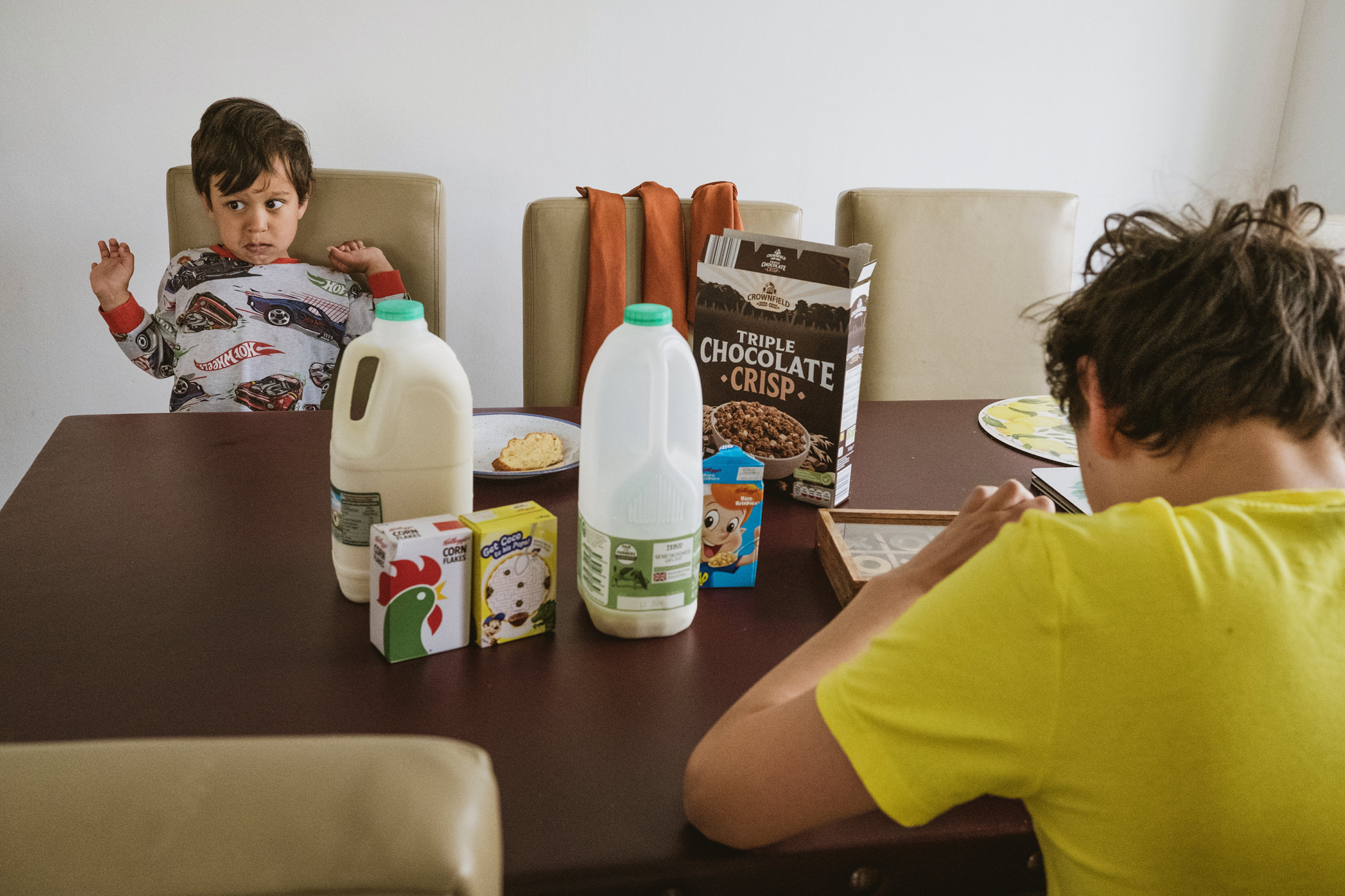 Children eating breakfast at table with milk and cereal.