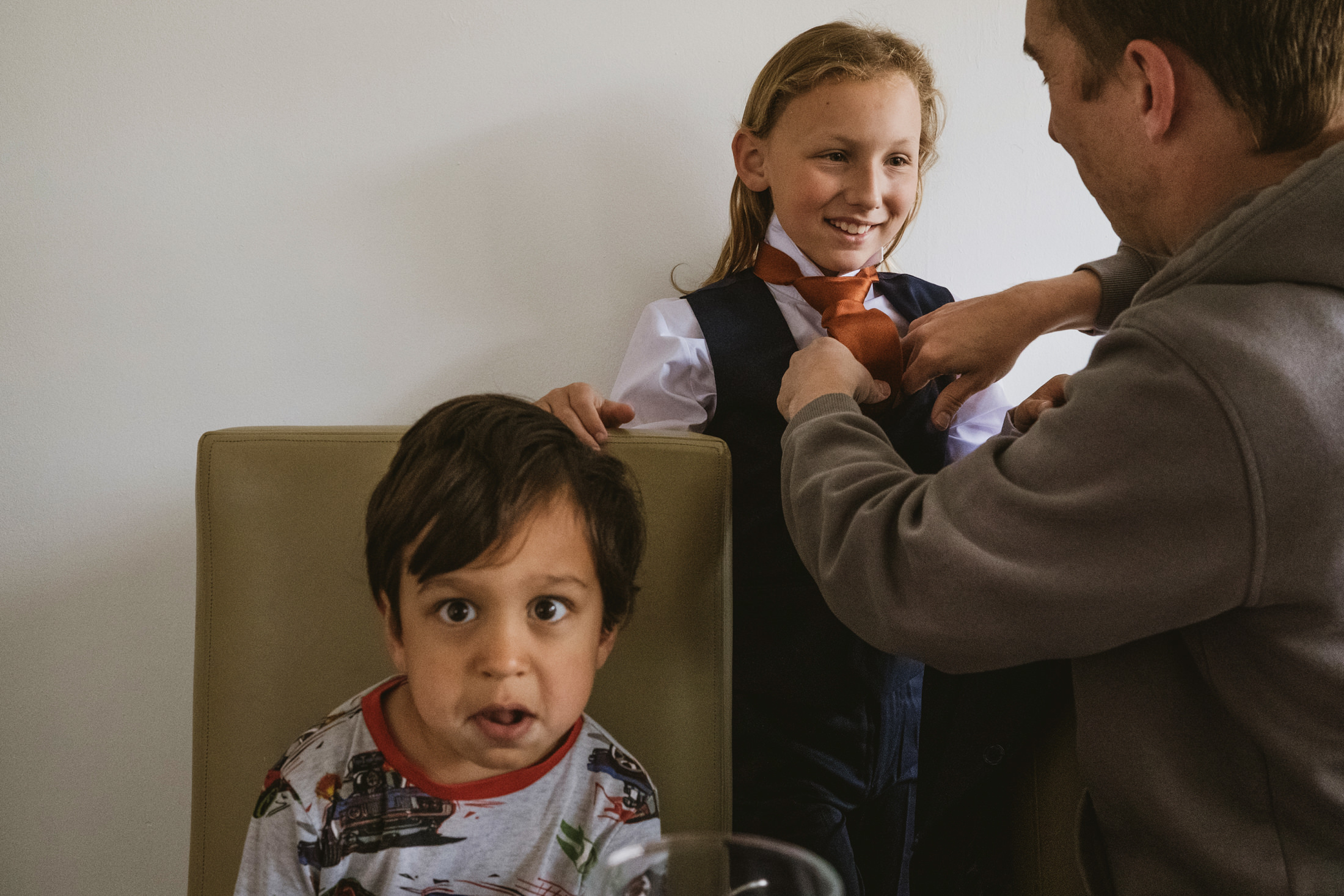 Man helps child with tie, another child watches.