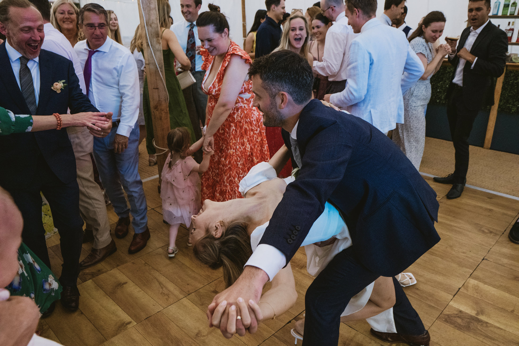 Guests laugh as groom dips bride on crowded dance floor during wedding reception documentary wedding photography