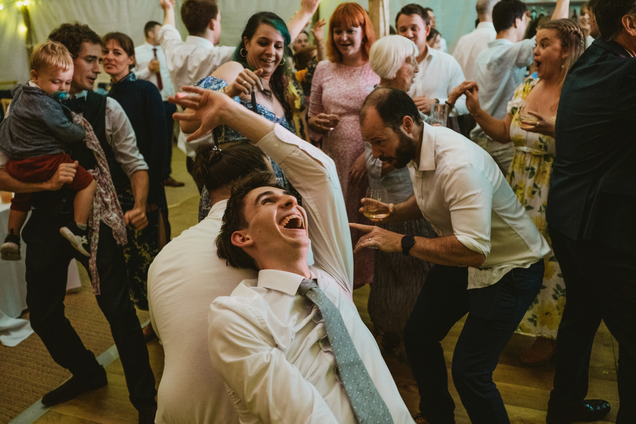 Guest laughing mid-dance, friends gathered around on a lively wedding reception dance floor.