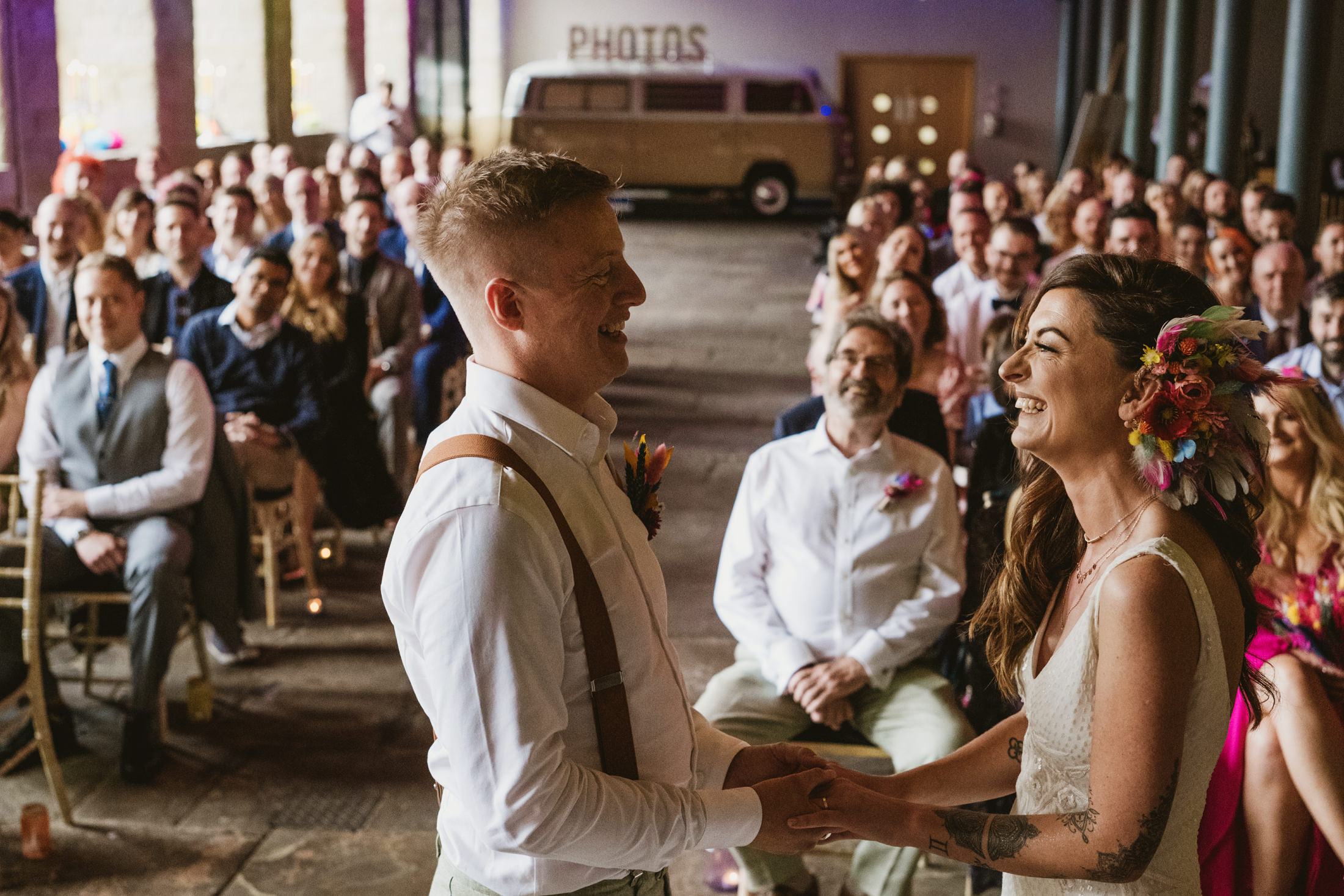 Bride and groom laughing during intimate wedding ceremony, guests watching warmly.
