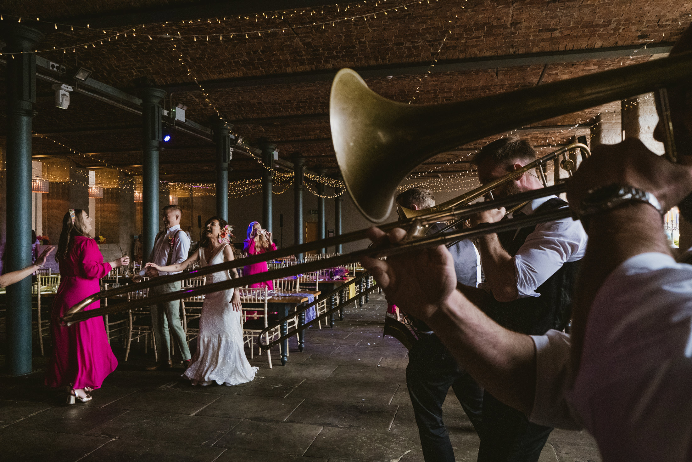 Bride laughing with guests as trombone plays at candlelit wedding reception.