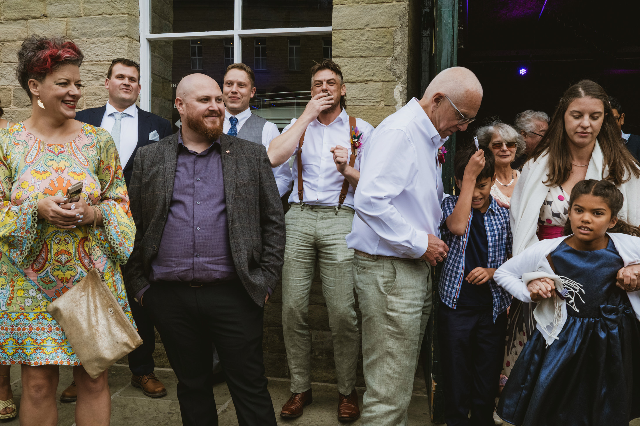 Wedding guests spill from a stone doorway, laughing and chatting together in documentary wedding photography.