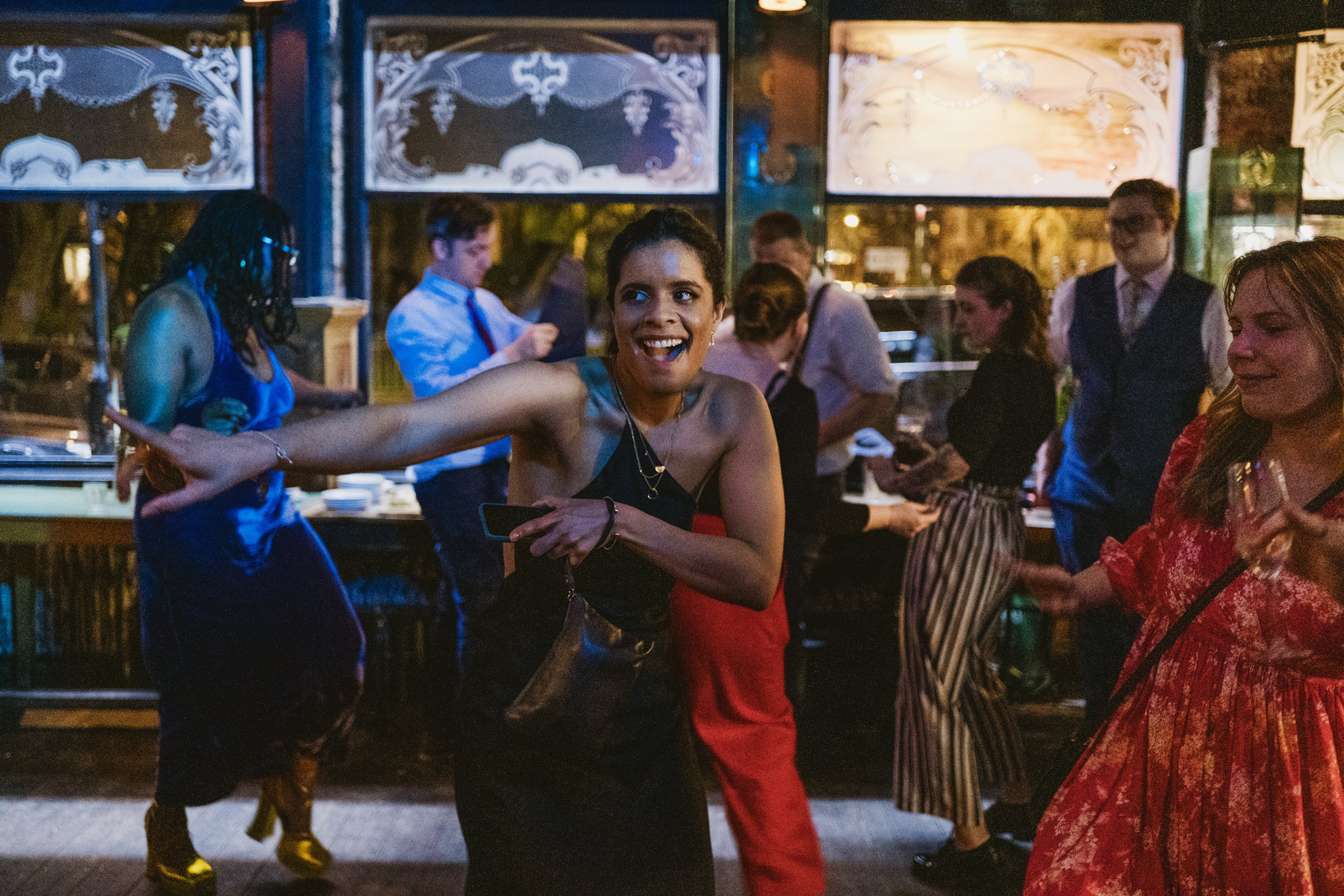 Guests dancing joyfully at a lively wedding reception, evening light glowing through windows behind them.