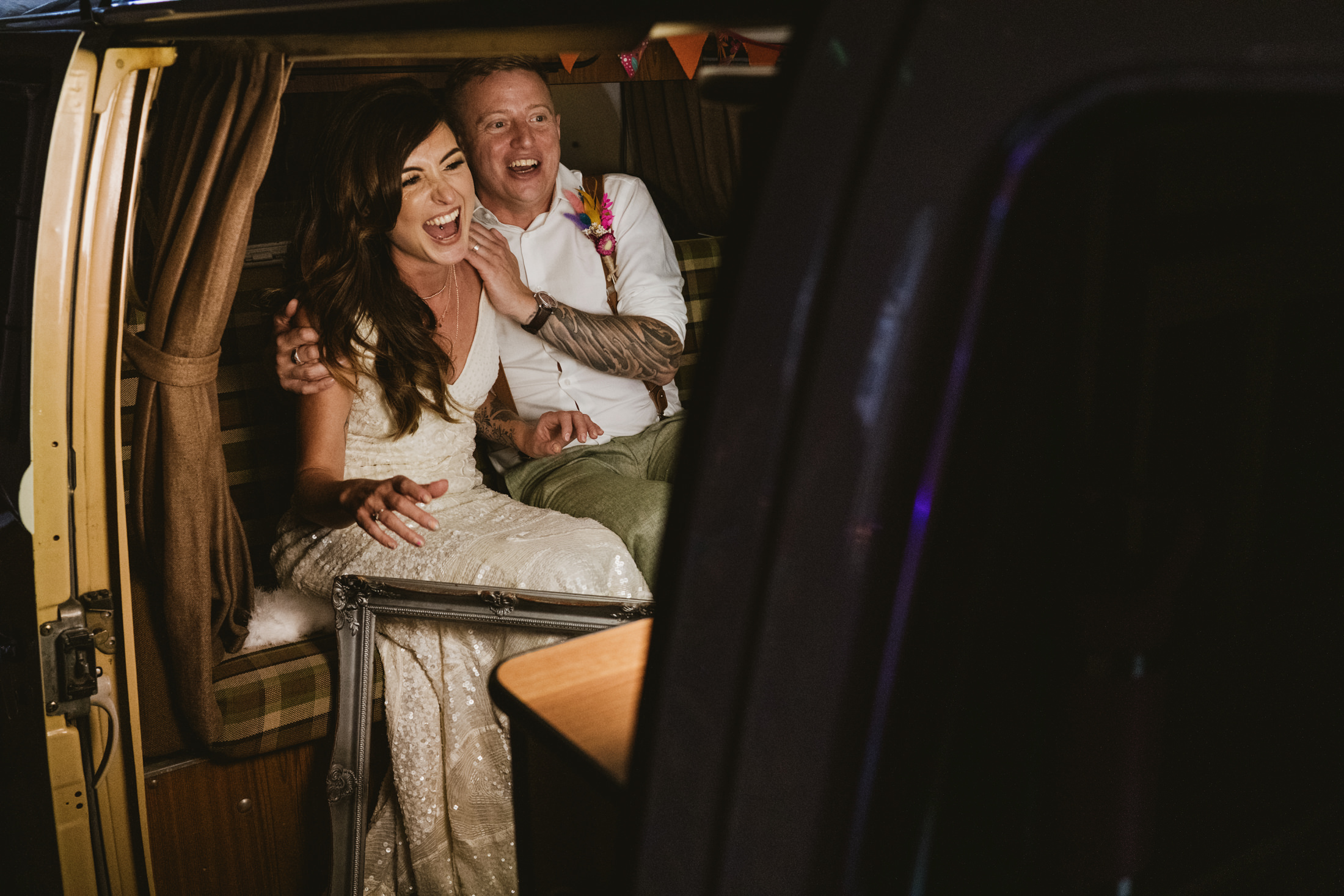 Bride and groom laughing inside vintage camper van during wedding reception, documentary wedding photography.