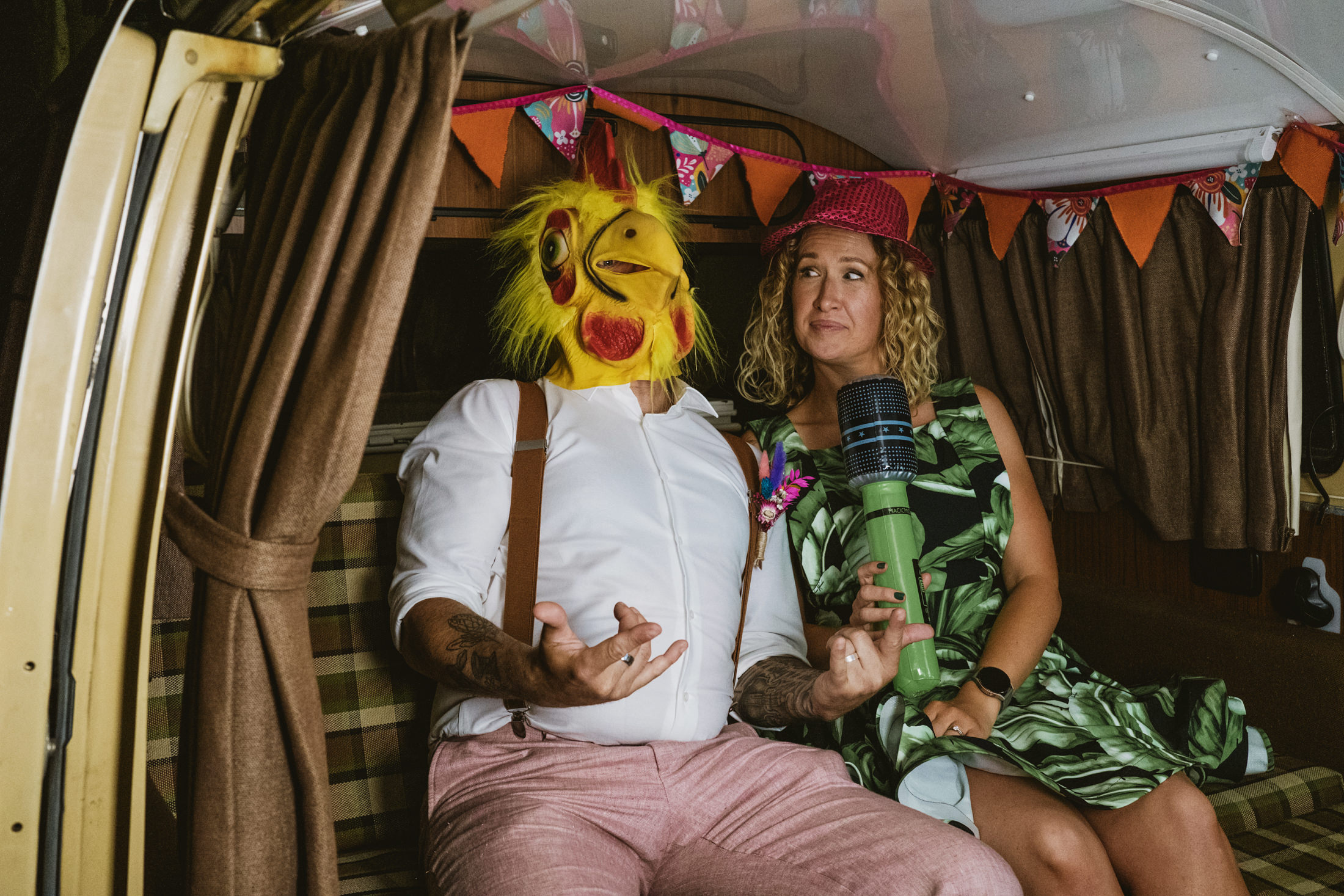 Guest in chicken mask beside woman with microphone inside campervan wedding photo booth.