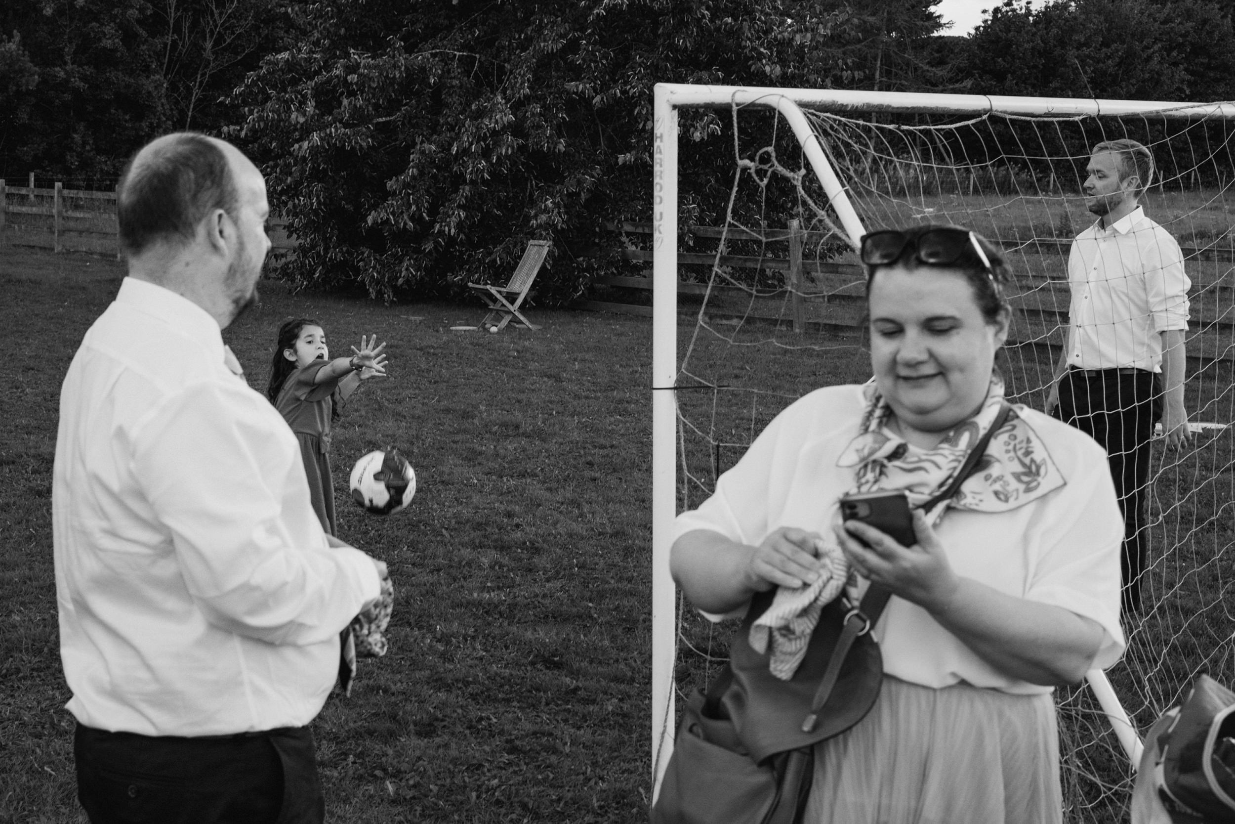 Group playing football in garden, one using phone.