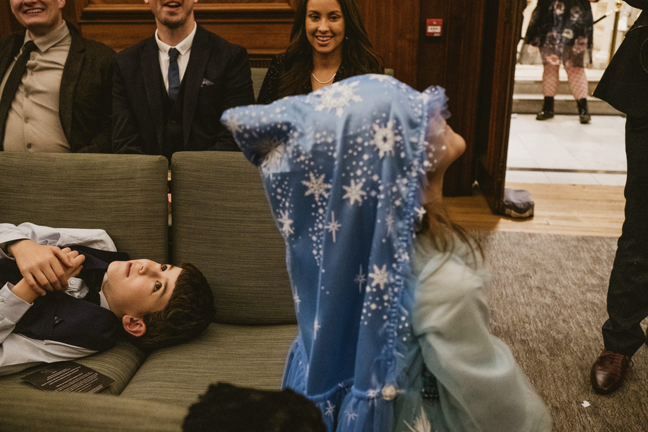 Children play with a blue starry blanket as guests laugh in a warm wedding ceremony room.
