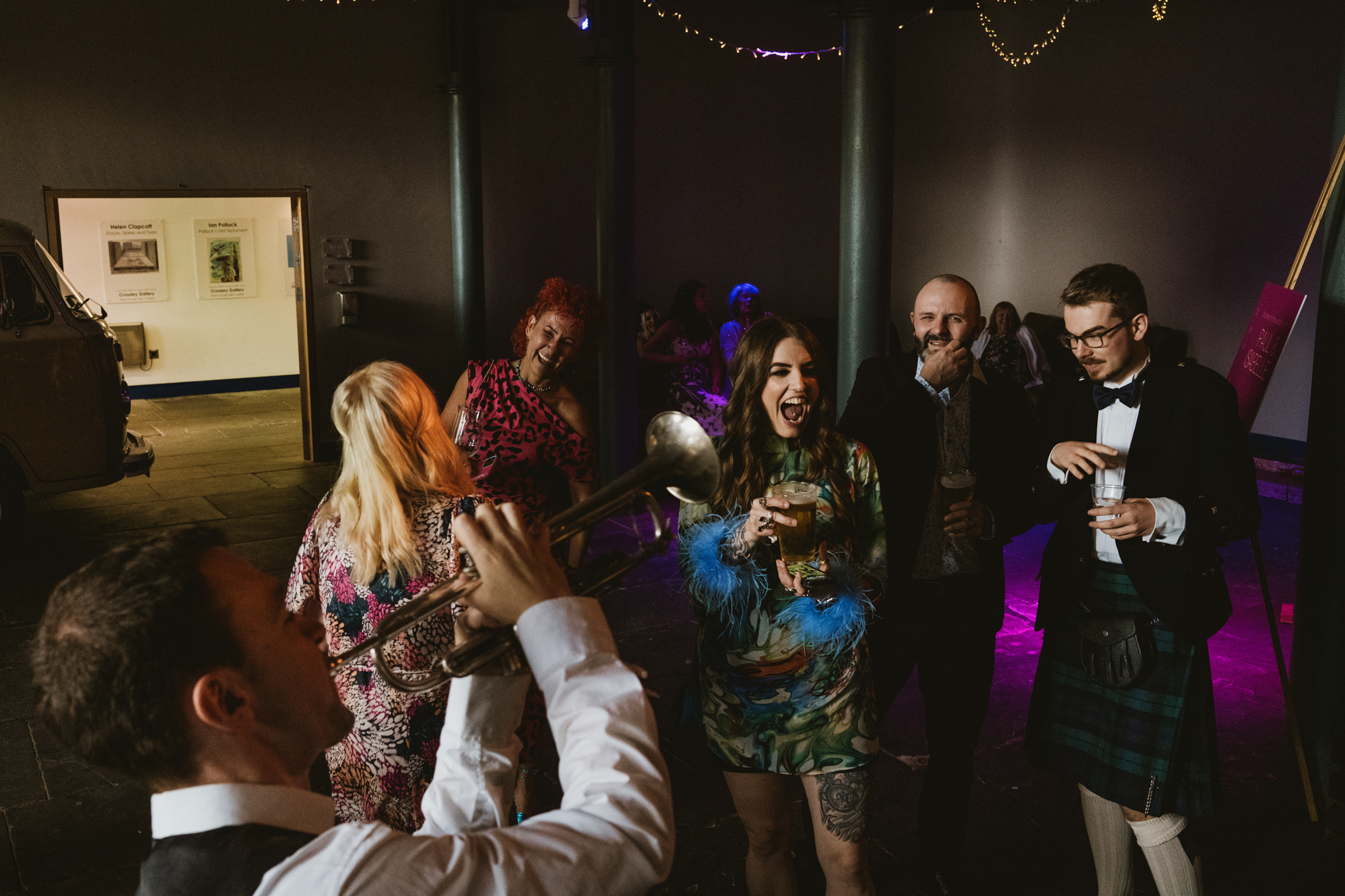 Trumpet player serenades laughing guests holding drinks on a glowing wedding reception dancefloor.