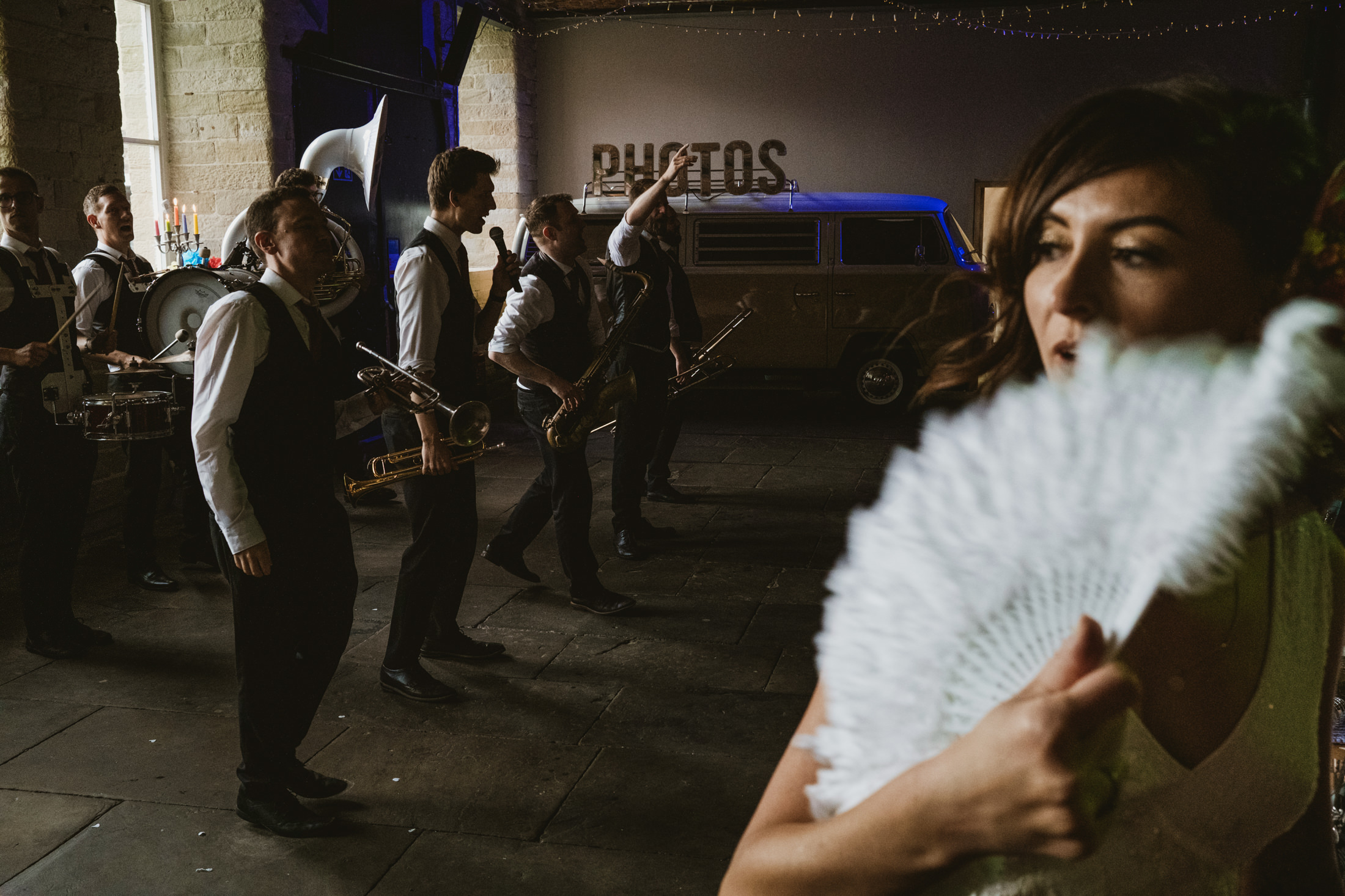 Brass band playing at wedding reception as woman cools herself with white fan.