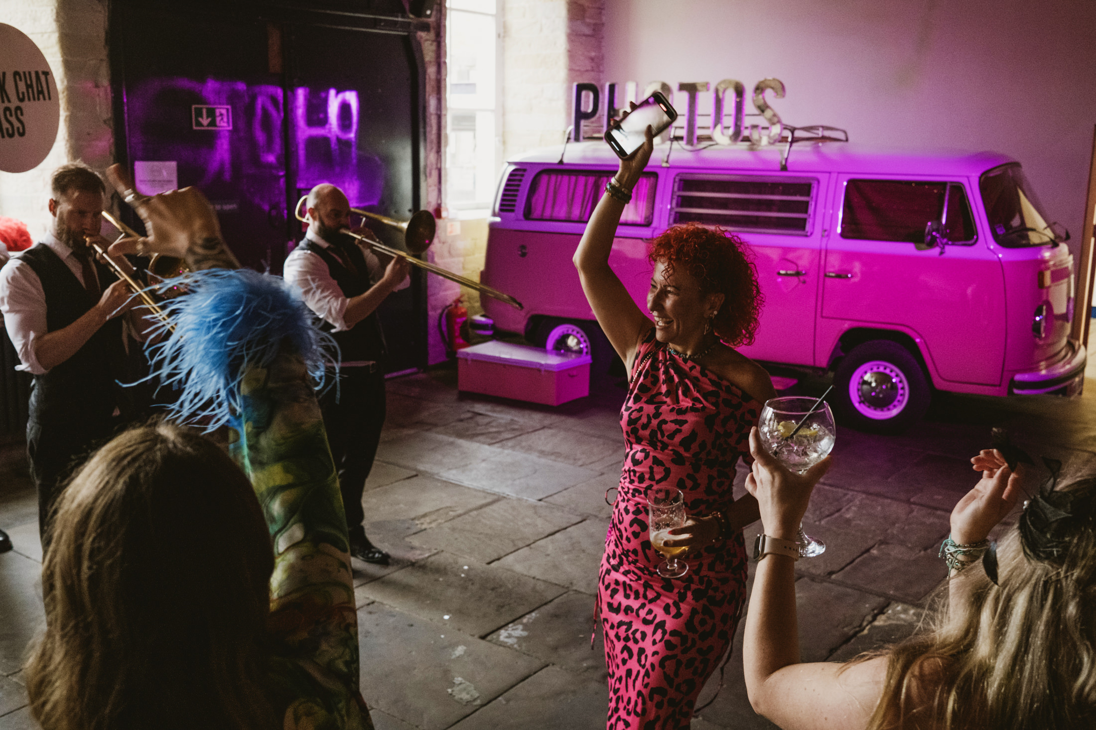 Guests dance as brass band plays beside pink van at lively wedding reception.